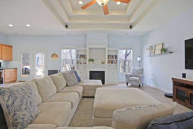 living room with a tray ceiling, a glass covered fireplace, recessed lighting, light tile patterned floors, and baseboards