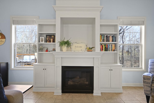 living room with light tile patterned floors, a glass covered fireplace, plenty of natural light, and baseboards