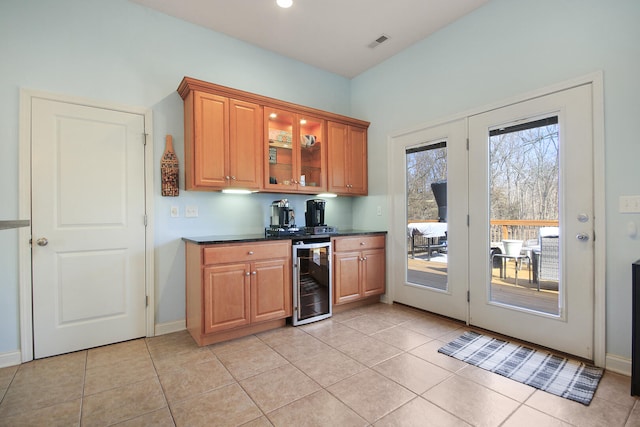 kitchen with visible vents, dark countertops, wine cooler, brown cabinetry, and glass insert cabinets