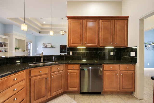 kitchen with dark stone countertops, a tray ceiling, a sink, dishwasher, and tasteful backsplash