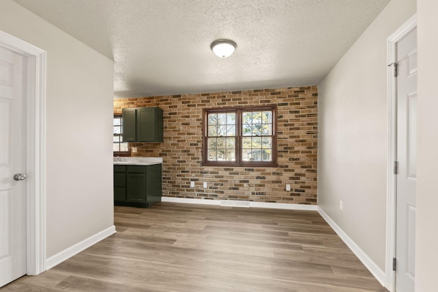 unfurnished dining area featuring light wood-style flooring, brick wall, a textured ceiling, and baseboards