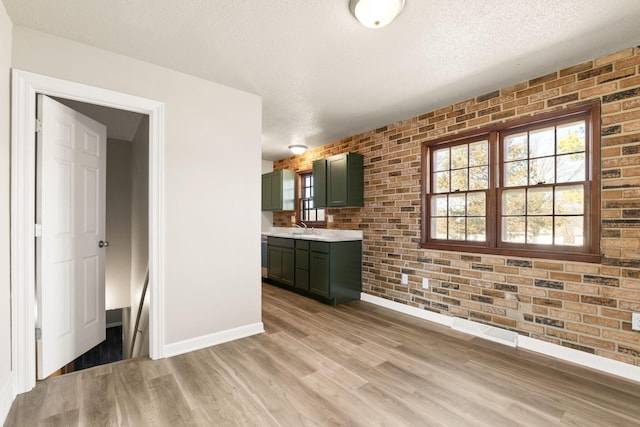 unfurnished dining area with baseboards, brick wall, a textured ceiling, and light wood-style floors