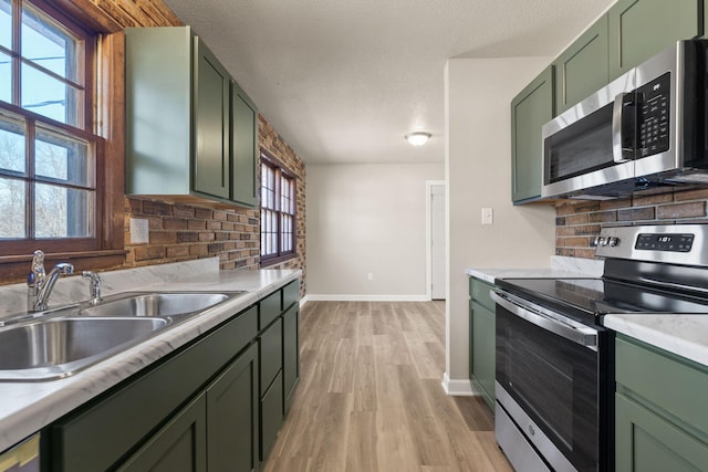 kitchen featuring stainless steel appliances, green cabinets, light countertops, and a sink