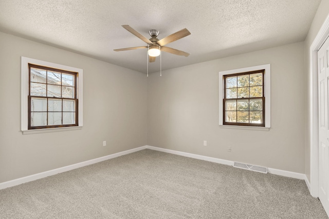 carpeted spare room with a wealth of natural light, visible vents, a ceiling fan, and baseboards