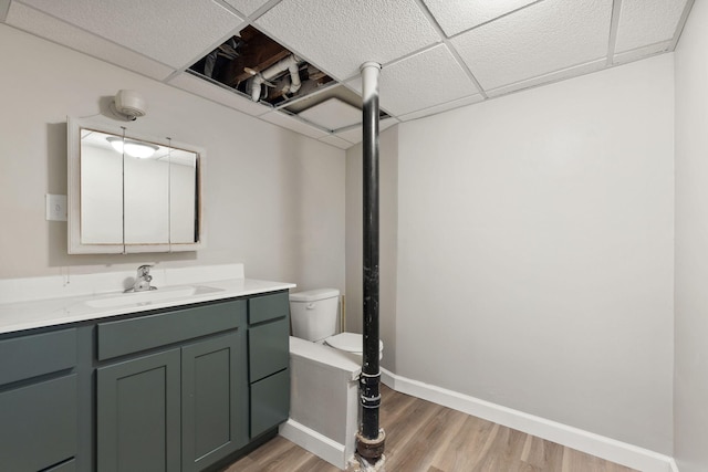 bathroom with toilet, a paneled ceiling, baseboards, and wood finished floors