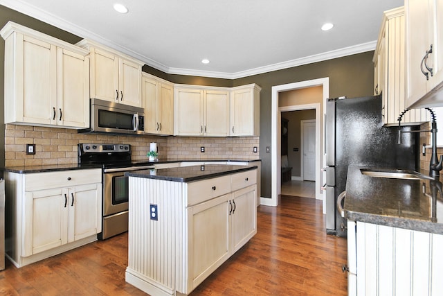 kitchen featuring ornamental molding, a kitchen island, wood finished floors, appliances with stainless steel finishes, and decorative backsplash