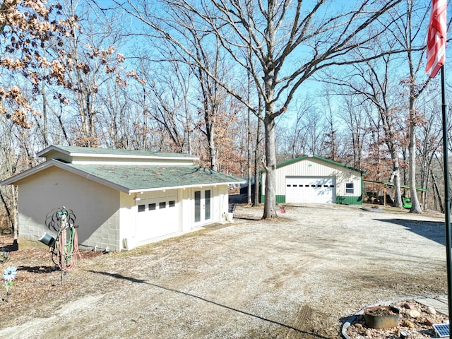 exterior space with an outbuilding, concrete block siding, a shingled roof, french doors, and a detached garage