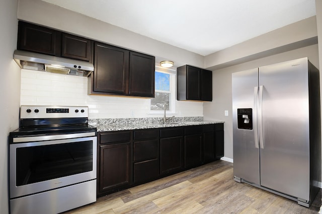 kitchen with backsplash, ventilation hood, light stone countertops, light wood-style flooring, and stainless steel appliances