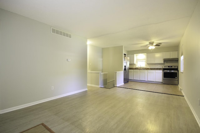 unfurnished living room featuring visible vents, a ceiling fan, a sink, light wood finished floors, and baseboards