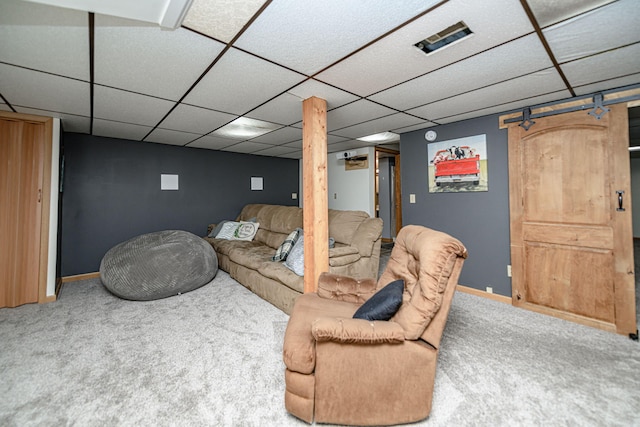 carpeted living room featuring a drop ceiling, baseboards, and a barn door