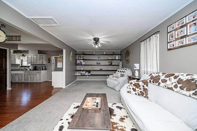 living area featuring visible vents, dark wood-type flooring, attic access, ornamental molding, and a textured ceiling