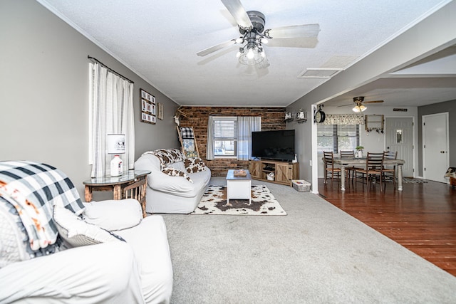 carpeted living area featuring brick wall, ceiling fan, attic access, ornamental molding, and a textured ceiling