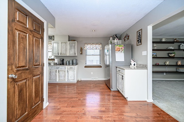 kitchen featuring visible vents, baseboards, light stone countertops, light wood-type flooring, and freestanding refrigerator