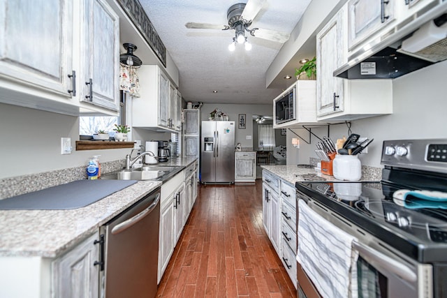 kitchen with under cabinet range hood, a sink, a textured ceiling, appliances with stainless steel finishes, and light countertops