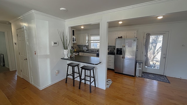 kitchen with stainless steel refrigerator with ice dispenser, a sink, dark countertops, a peninsula, and white cabinets