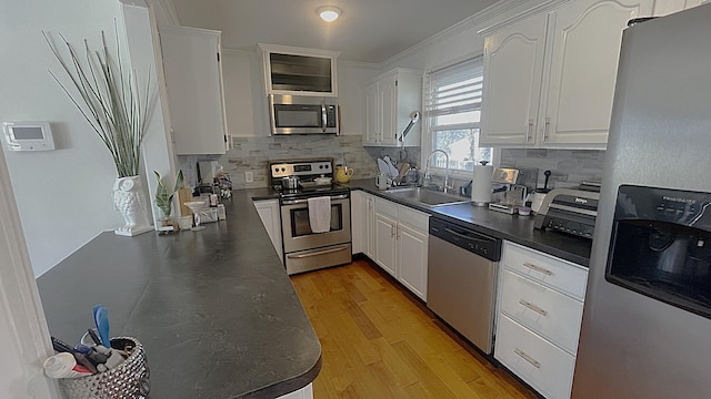 kitchen with light wood finished floors, a sink, stainless steel appliances, white cabinets, and dark countertops