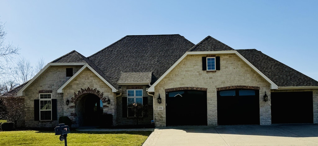 view of front of house featuring a shingled roof, a front lawn, concrete driveway, stone siding, and an attached garage