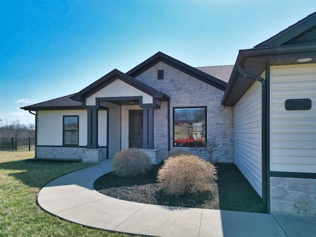 view of front of house featuring stone siding, a shingled roof, a front lawn, and fence