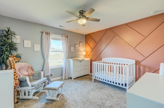 bedroom featuring visible vents, ceiling fan, a crib, and carpet