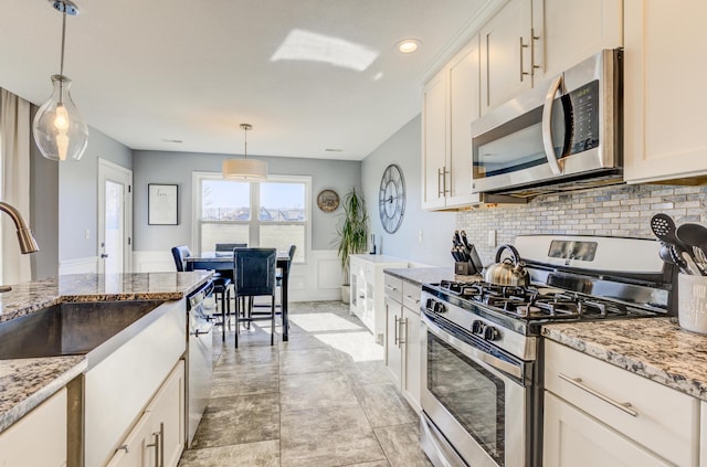 kitchen featuring wainscoting, backsplash, stainless steel appliances, and light stone countertops