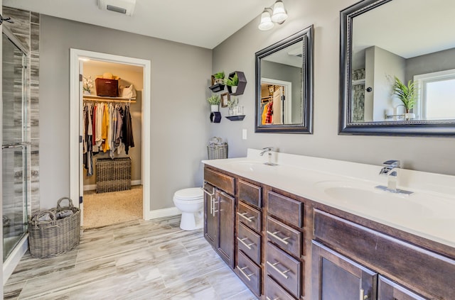 full bath featuring double vanity, a shower with shower door, toilet, and a sink