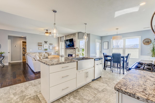 kitchen with a sink, light stone counters, open floor plan, white cabinets, and dishwasher