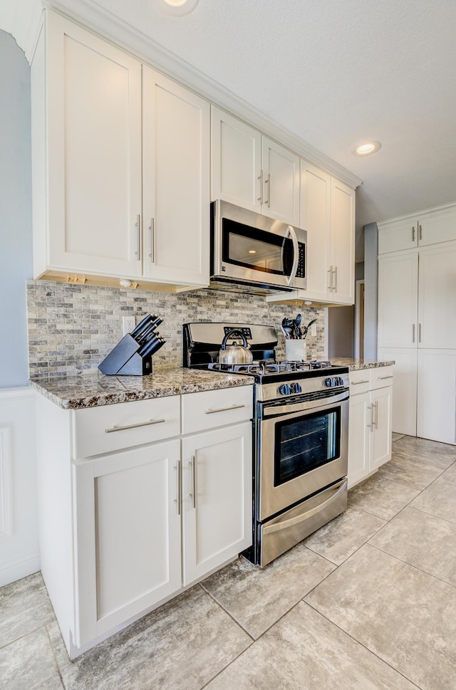 kitchen featuring light stone counters, decorative backsplash, appliances with stainless steel finishes, and white cabinets