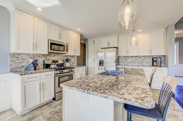 kitchen featuring light stone counters, a kitchen island with sink, a sink, white cabinets, and appliances with stainless steel finishes