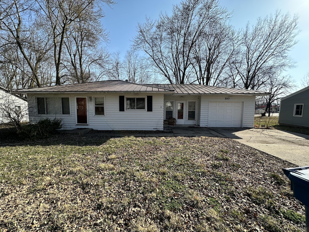 ranch-style house featuring an attached garage, driveway, and metal roof