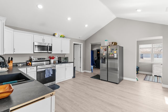 kitchen with a sink, stainless steel appliances, dark countertops, and white cabinetry