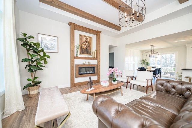 living area featuring wood finished floors, baseboards, a tray ceiling, a high end fireplace, and a notable chandelier