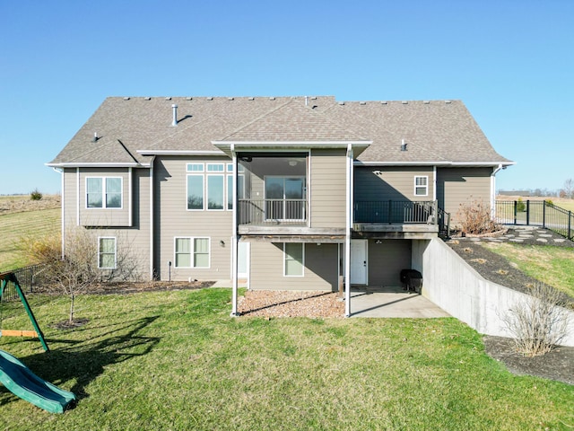 rear view of house with a playground, a patio area, a lawn, and roof with shingles