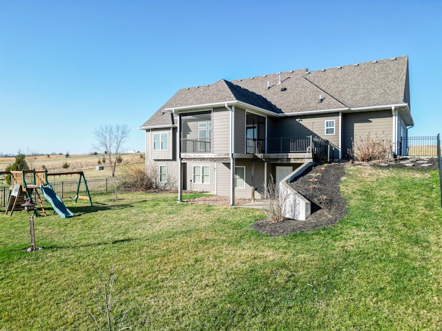 rear view of property with a lawn, a shingled roof, a playground, and fence