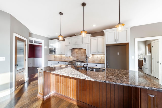 kitchen with dark wood finished floors, washer / clothes dryer, a sink, white cabinets, and stainless steel microwave