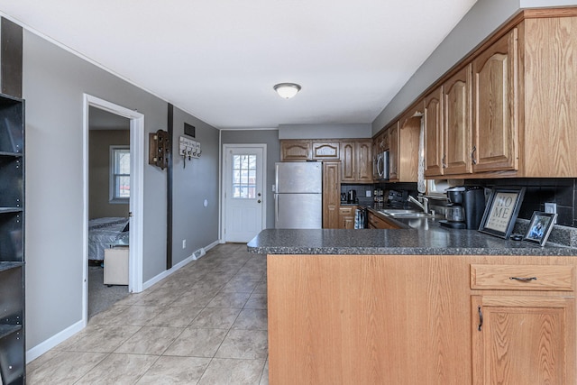 kitchen featuring a peninsula, light tile patterned flooring, a sink, stainless steel appliances, and dark countertops