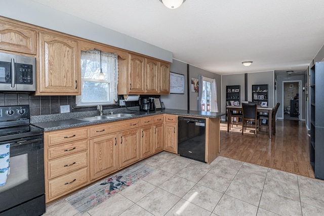 kitchen featuring a peninsula, light tile patterned flooring, a sink, black appliances, and dark countertops