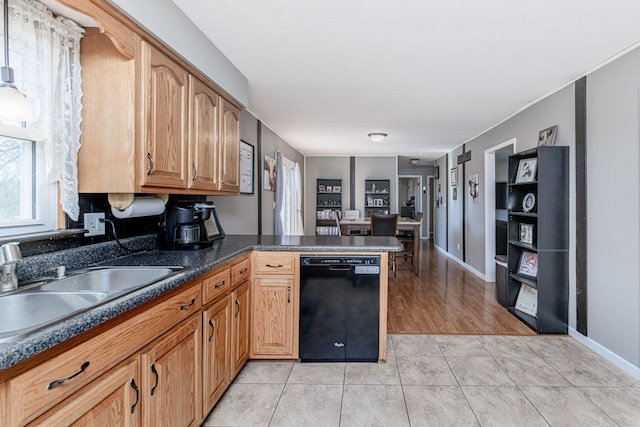 kitchen with dark countertops, black dishwasher, light tile patterned floors, a peninsula, and a sink