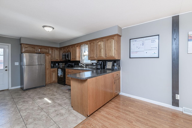 kitchen featuring a sink, dark countertops, appliances with stainless steel finishes, a peninsula, and baseboards