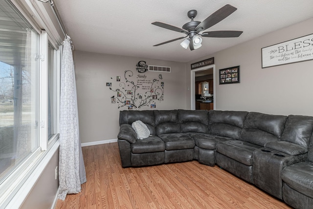 living area with baseboards, visible vents, ceiling fan, light wood-style floors, and a textured ceiling