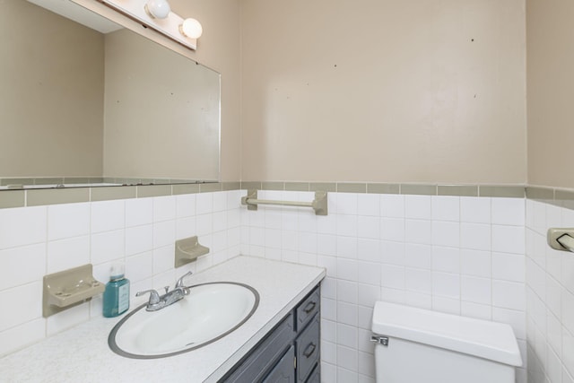 bathroom featuring tile walls, wainscoting, toilet, and vanity