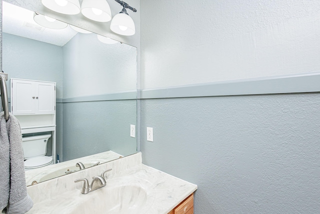 half bathroom with toilet, vanity, and a textured wall