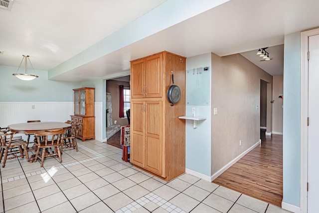 kitchen featuring visible vents, light tile patterned flooring, wainscoting, baseboards, and hanging light fixtures