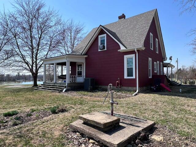 exterior space with central air condition unit, a yard, covered porch, a shingled roof, and a chimney