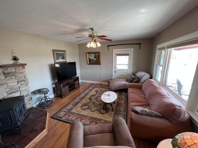 living room featuring ceiling fan, baseboards, wood finished floors, and a wood stove