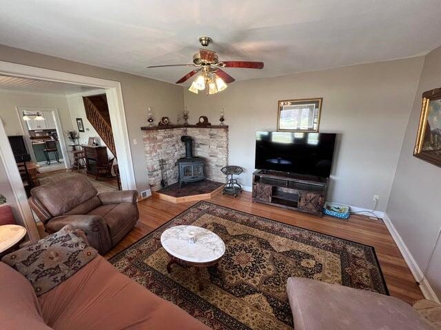 living room with stairs, a wood stove, wood finished floors, and a ceiling fan