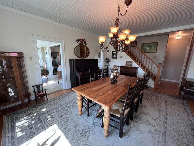 dining room with baseboards, stairs, ornamental molding, wood finished floors, and a notable chandelier