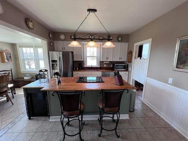 kitchen featuring light tile patterned floors, a wainscoted wall, stainless steel appliances, pendant lighting, and white cabinetry