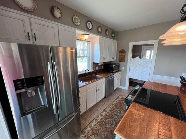 kitchen featuring a sink, backsplash, white cabinetry, appliances with stainless steel finishes, and baseboards