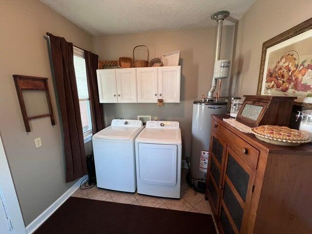 laundry room featuring a textured ceiling, washing machine and dryer, gas water heater, cabinet space, and light tile patterned floors