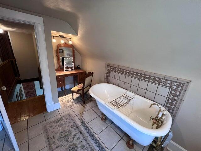 bathroom with tile patterned flooring, baseboards, a freestanding bath, vanity, and vaulted ceiling